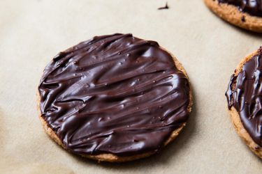 A vegan chocolate-covered digestive biscuit resting on parchment paper. There are two other biscuits on the right periphery of the image.