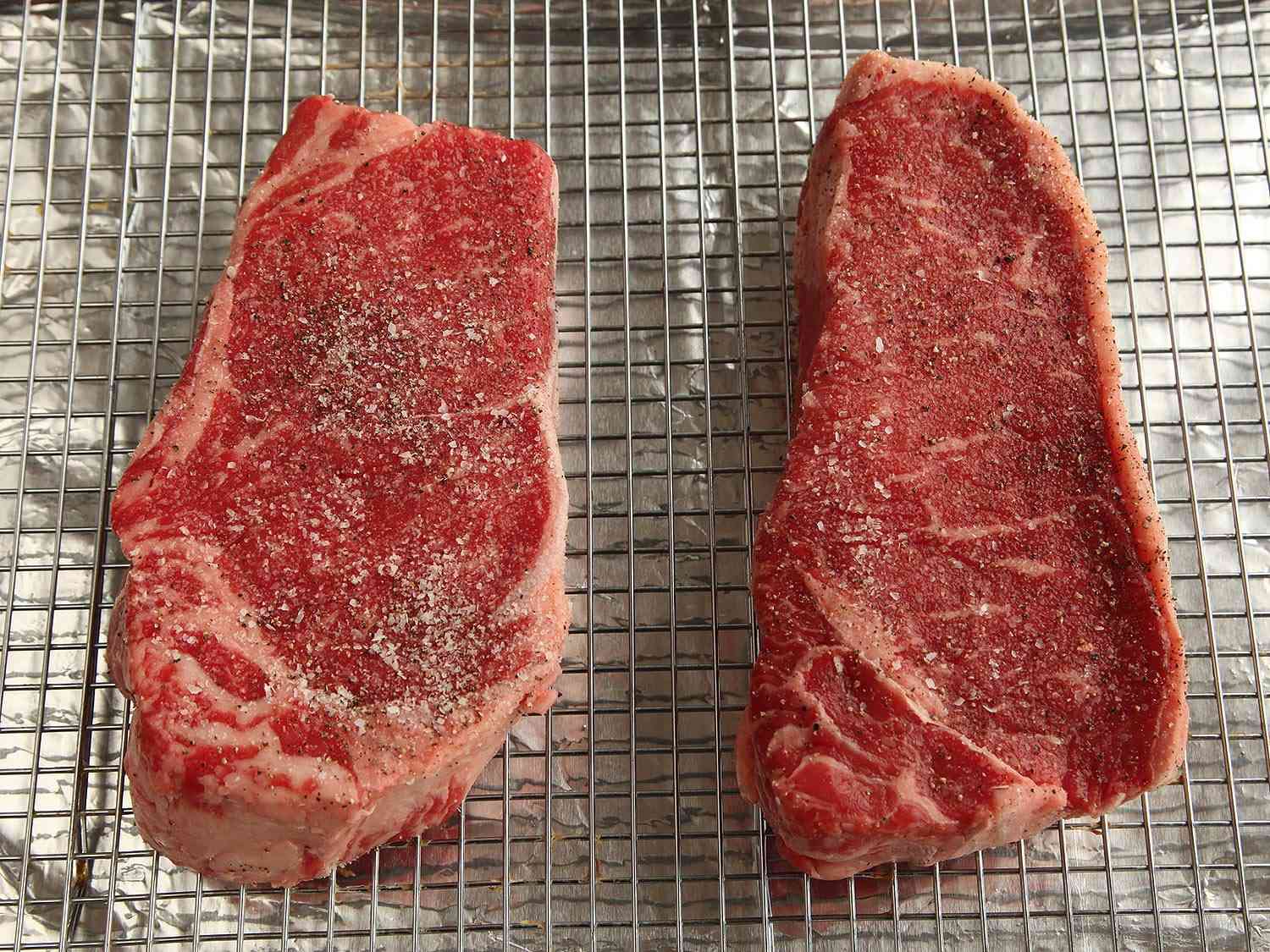 两块厚厚的调味牛排放在铁丝架上，放在带边的烤盘上