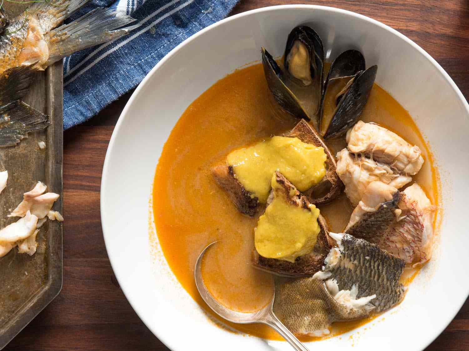 A top down view of a bowl of bouillabaisse, topped with mussels, pieces of fish, and rouille.