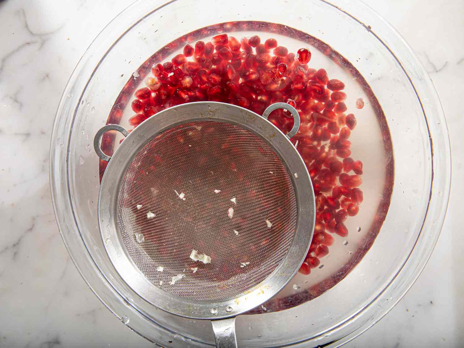 Overhead view of removing pith from water with pomegranate seeds