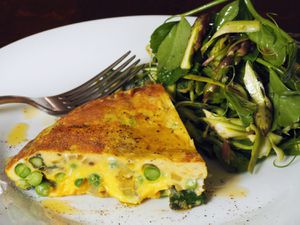 A slice of asparagus-sweet pea frittata, served on a plate with a minty spring salad.