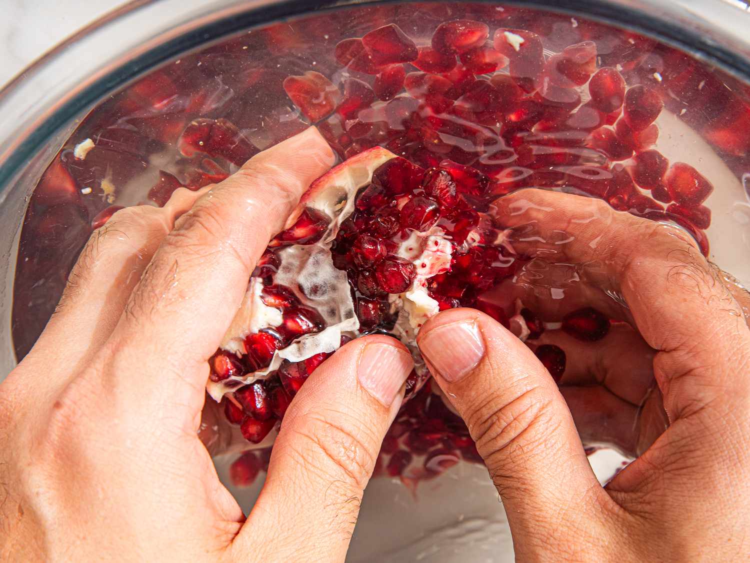 Overhead view of pushing seeds of a pomegranate out of pith into a bowl of water