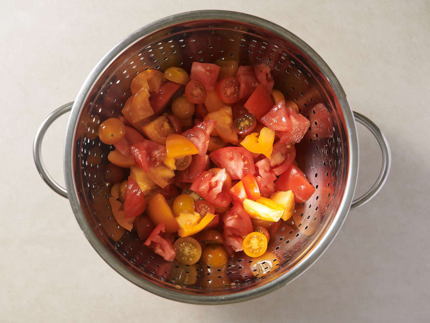 Chopped tomatoes seasoned with kosher salt inside a colander set over a bowl