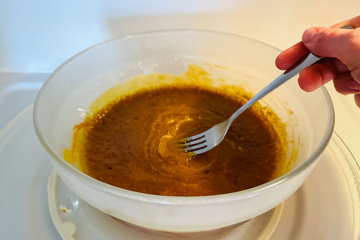 一只手用叉子在微波炉里搅拌任何一天的菜里的酱汁