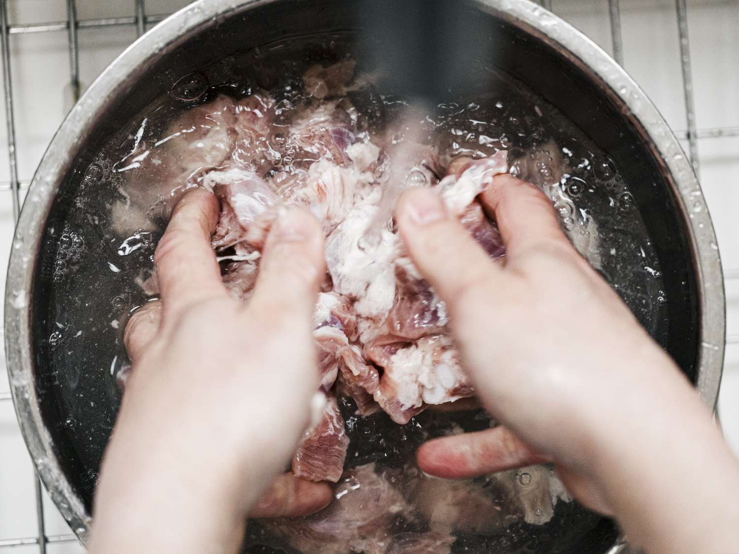 用手在水龙头下用力清洗碗里的猪肉＂width=