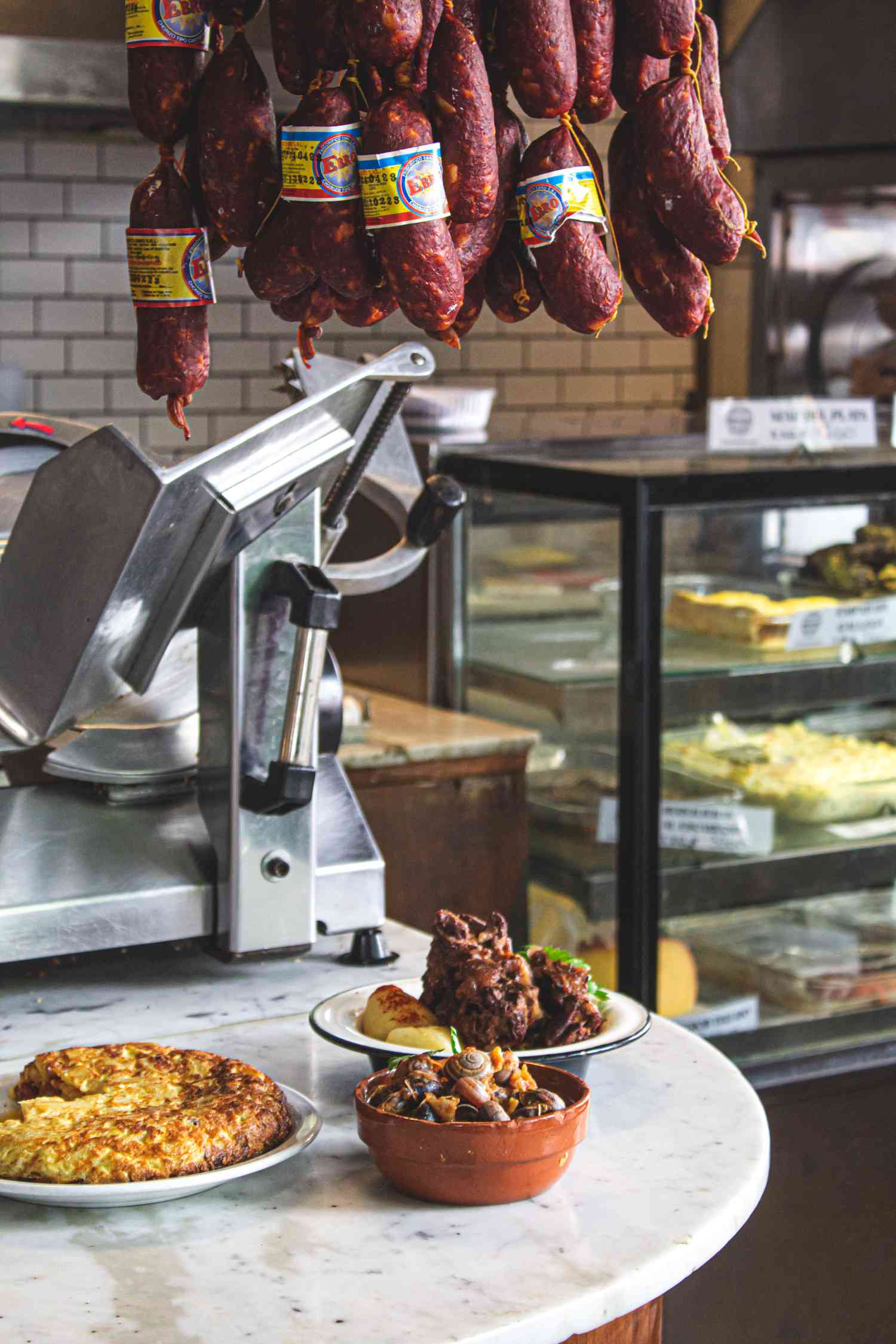 Vertical view of dishes on a counter with a meta slicer behind and sausages hanging from the ceiling