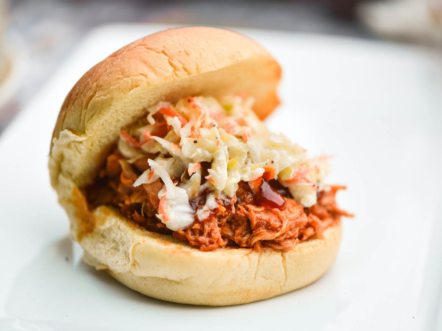 A sandwich bun filled with barbecue pulled chicken and coleslaw