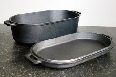 a cast iron roasting pan and lid sit on a counter side by side