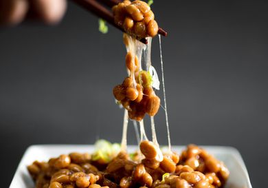 筷子夹着纳豆放在方形盘子上，纳豆是一种发酵的大豆，是日本常见的早餐。