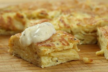 A slice of s salt-and-vinegar Spanish tortilla resting on a cutting board, topped with quick cheaty allioli.