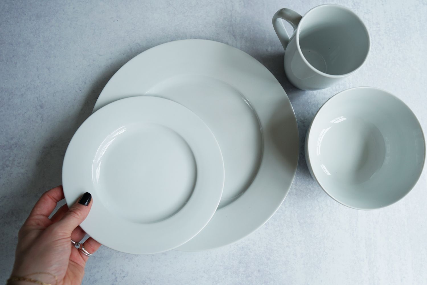 a person putting a white salad plate onto a white dinner plate