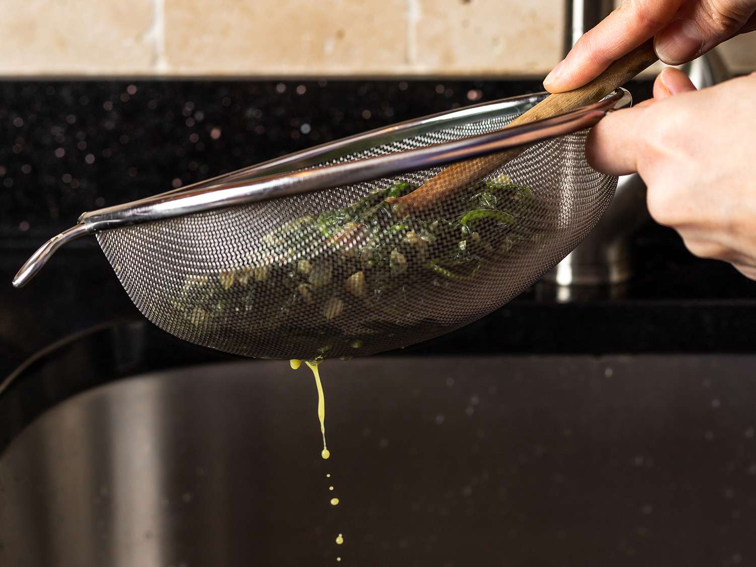 用细孔滤网将菠菜中的液体沥干，用锅铲压在上面以提取更多的液体。