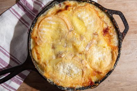 A cast iron skillet full to the brim with melted and browned soft-rind cheese.