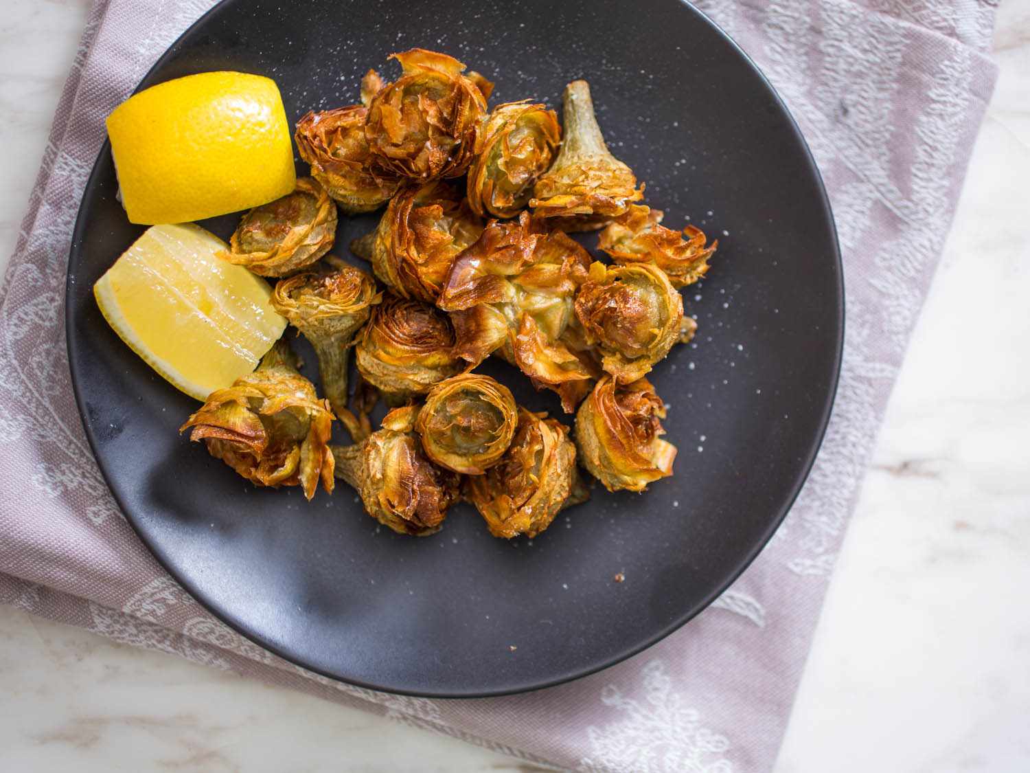 Overhead view of fried artichoke hearts plattered with lemon wedges.