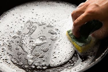 Cleaning a cast iron pan with warm, soapy water.