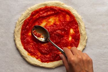 纽约式披萨酱，用金属勺子抹在生的披萨面团上。