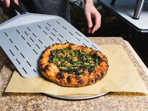Sliding a charred broccoli rabe pizza onto a serving tray