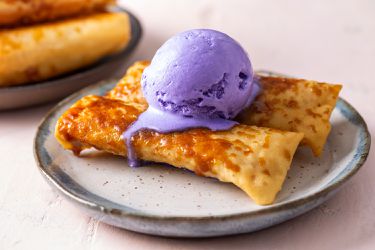 two turon on a plate with a scoop of ube ice cream dripping down the side