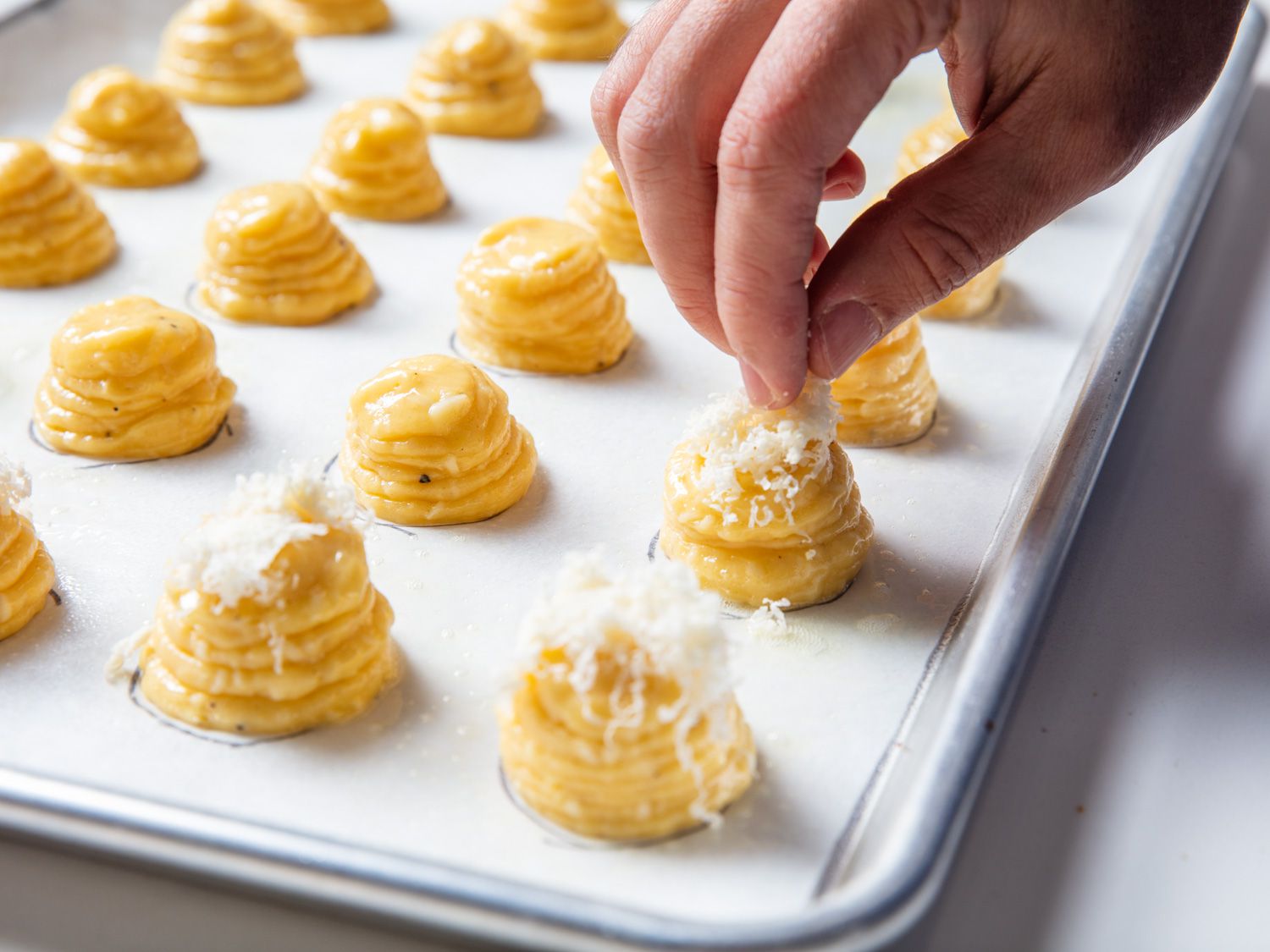 A pinch of finely grated cheese is added to each choux paste mound.