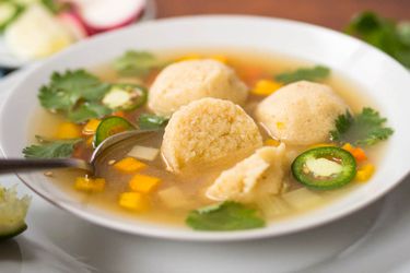 A bowl of masa-ball soup garnished with sliced jalapeño and cilantro.