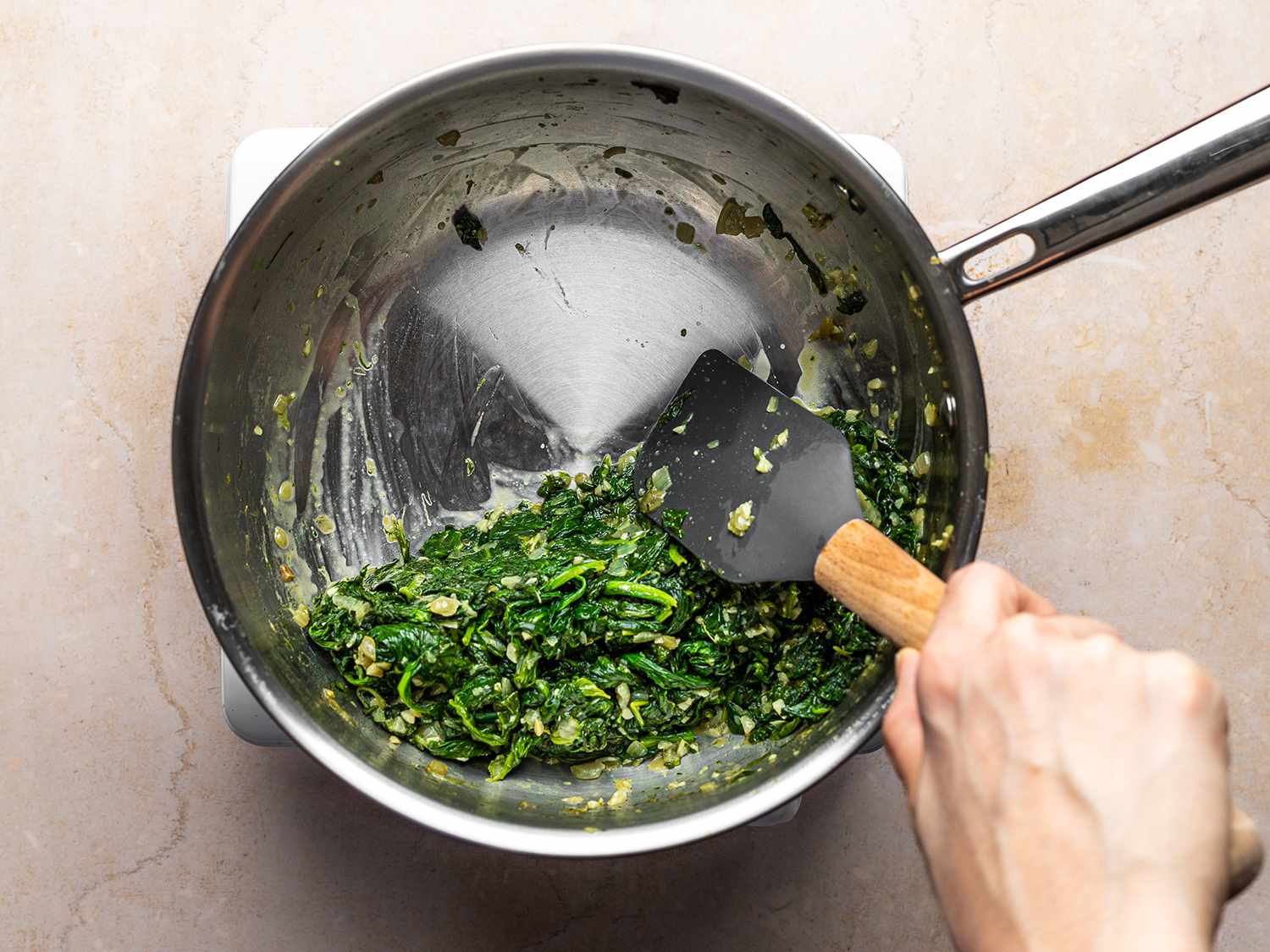 The blanched spinach, being mixed with a spatula in a saucepan.