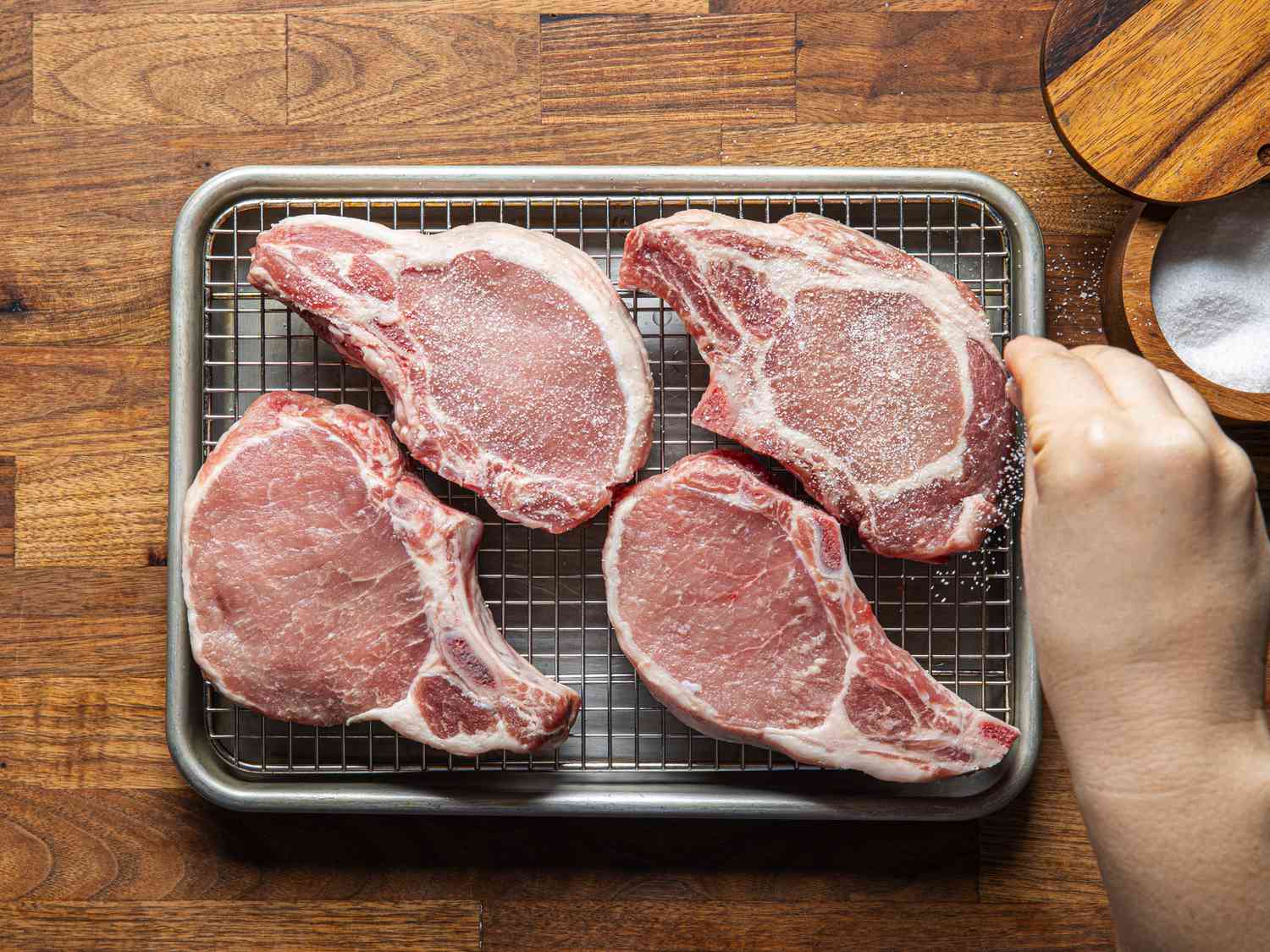 Overhead view of sprinkling pork chops with salt