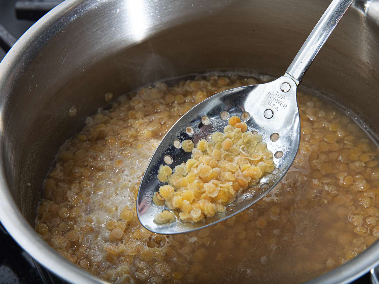 Cooked lentils being lifted out of a pot with a slotted spoon