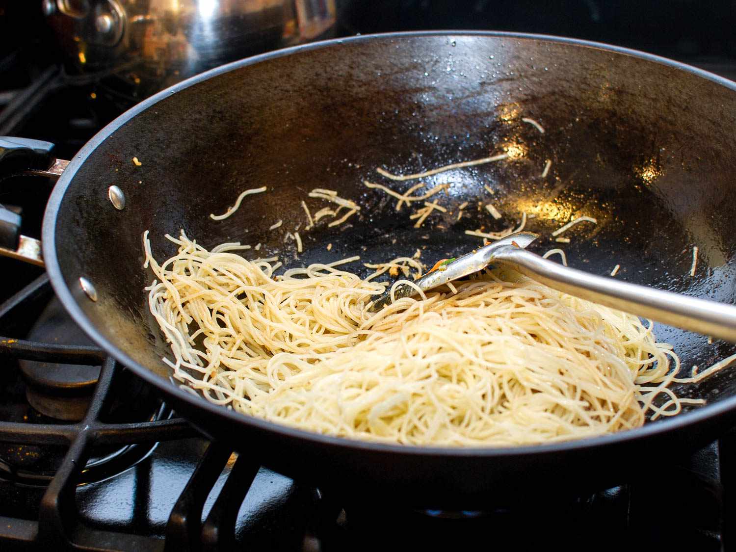 Spatula stirring softened rice vermicelli noodles in a hot wok.