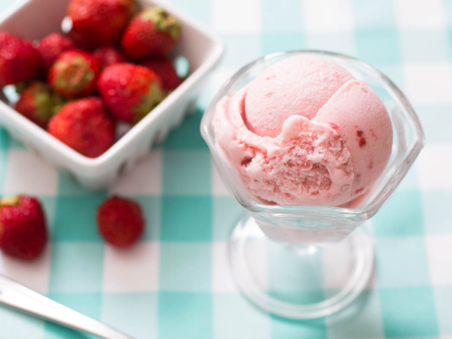 一勺草莓冰淇淋放在一个有脚的玻璃盘子里，旁边是一个草莓容器。