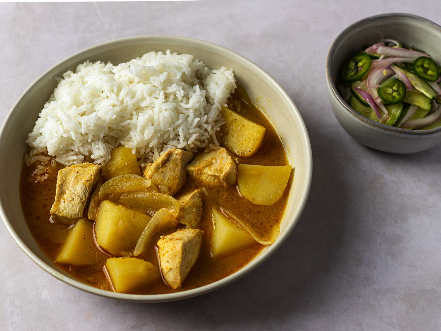 A ceramic bowl holding the chicken curry and rice, with another smaller bowl on the right hand side holding the vegetable salad.
