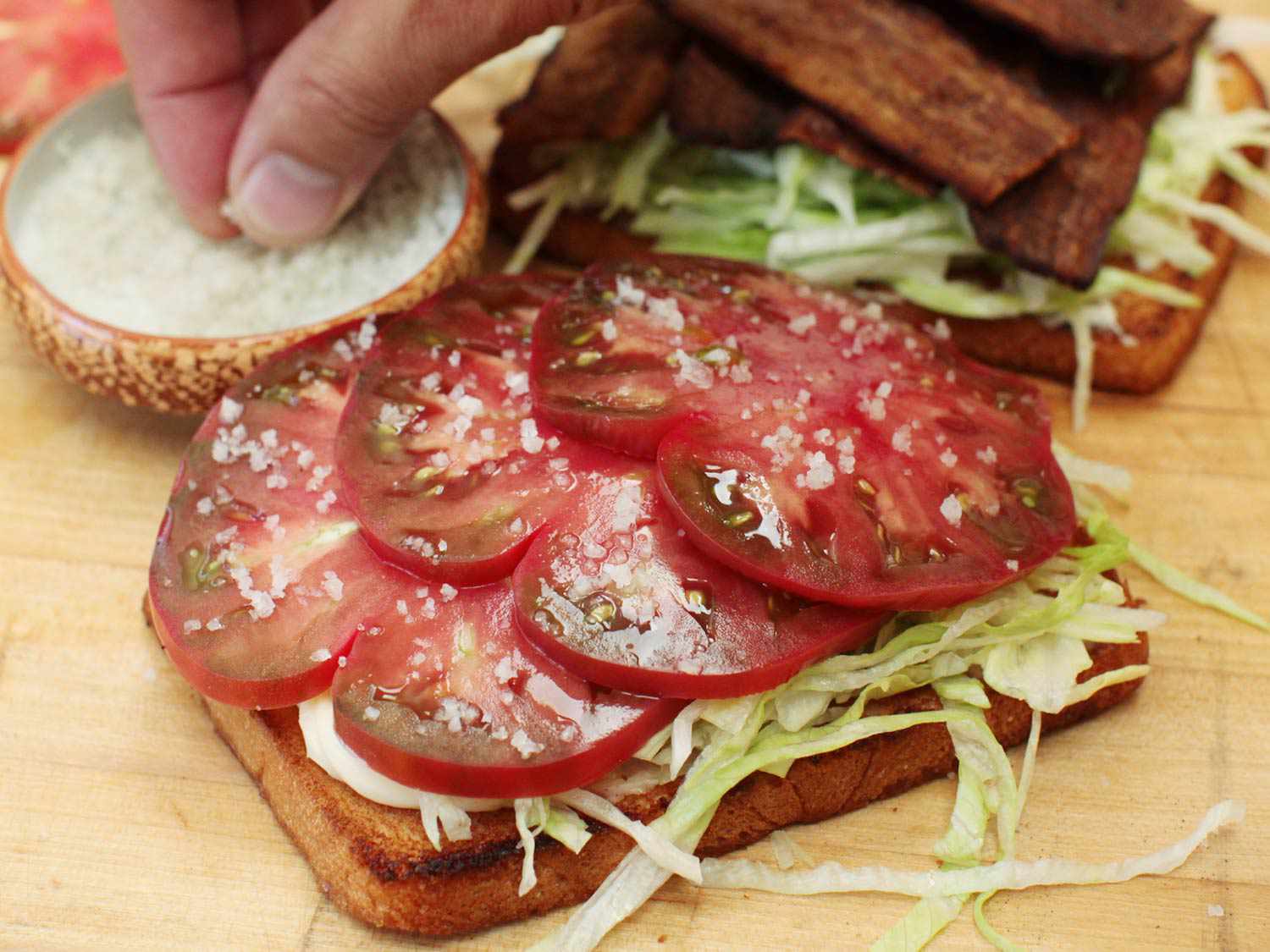 番茄片撒上盐，分层在生菜上，放在一片烤三明治面包上