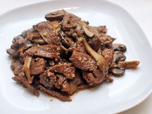 A white plate with a pile of stir-fried beef and mushrooms.