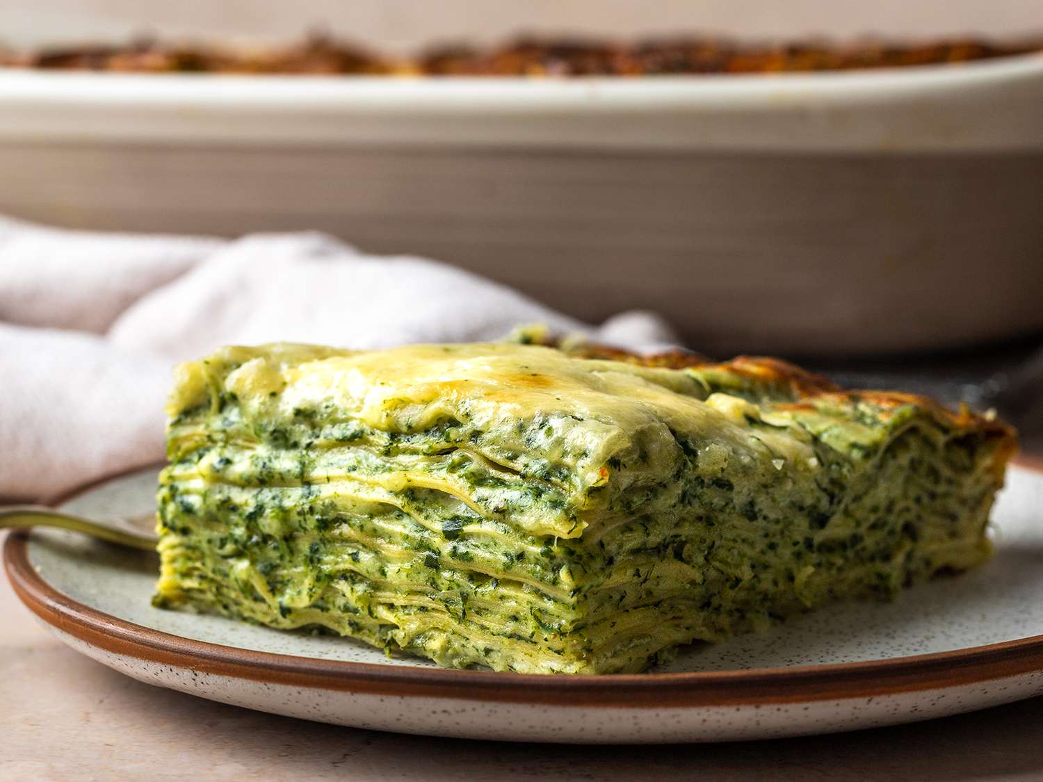A slice of spinach lasagna, shot from the side so that all of the layers are visible.