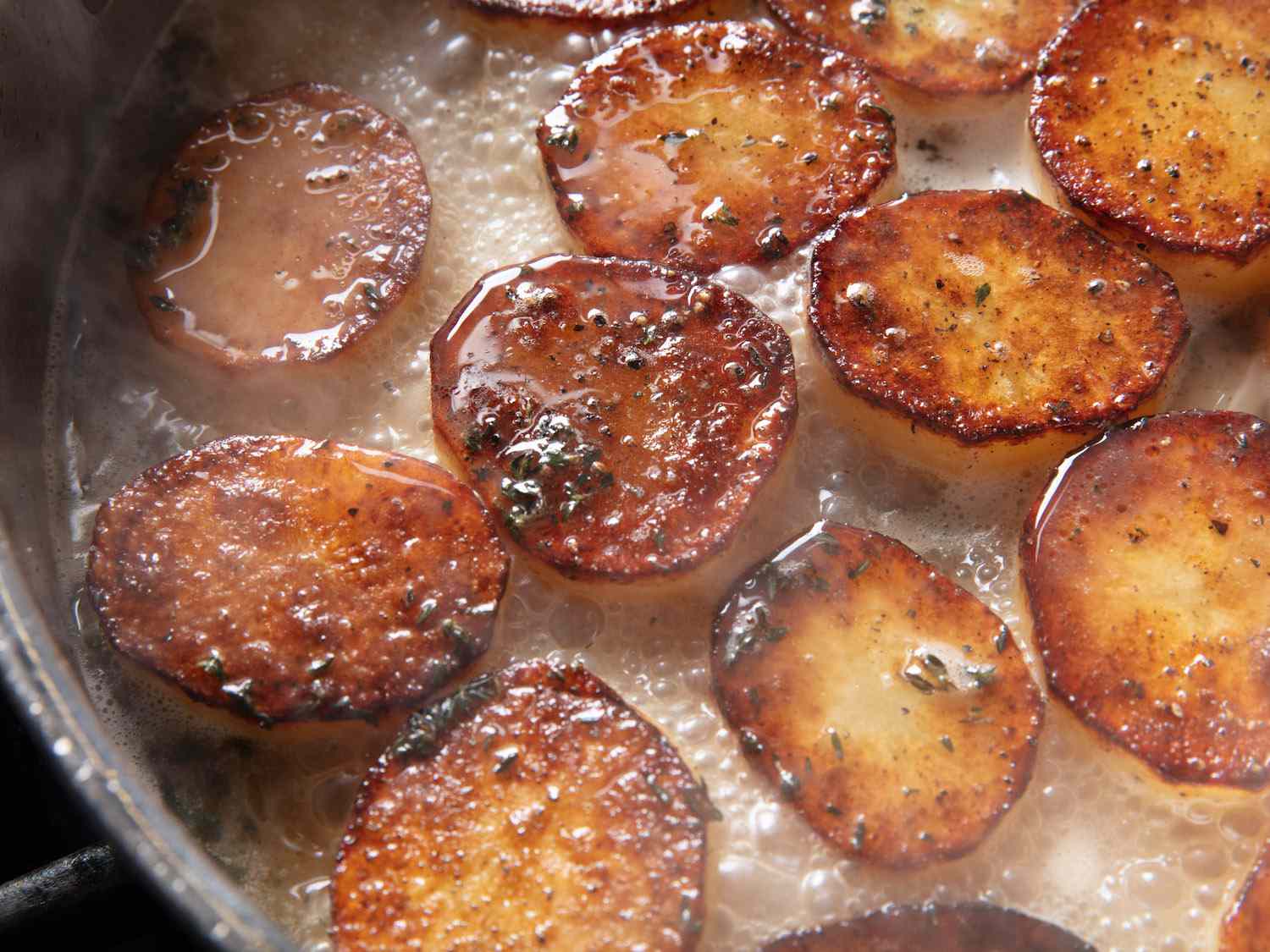 特写土豆在锅中与高汤，黄油，百里香和大蒜煨