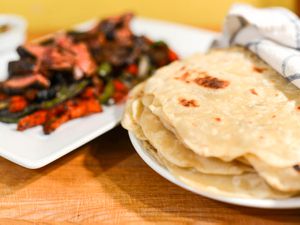 stack of thin flour tortilla next to a platter of steak fajita