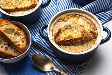 Overhead view of two bowls of french onion soup in small bowls on a striped blue background