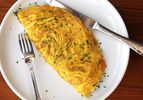 A large, diner-style omelette sprinkled with chopped chives on a plate.