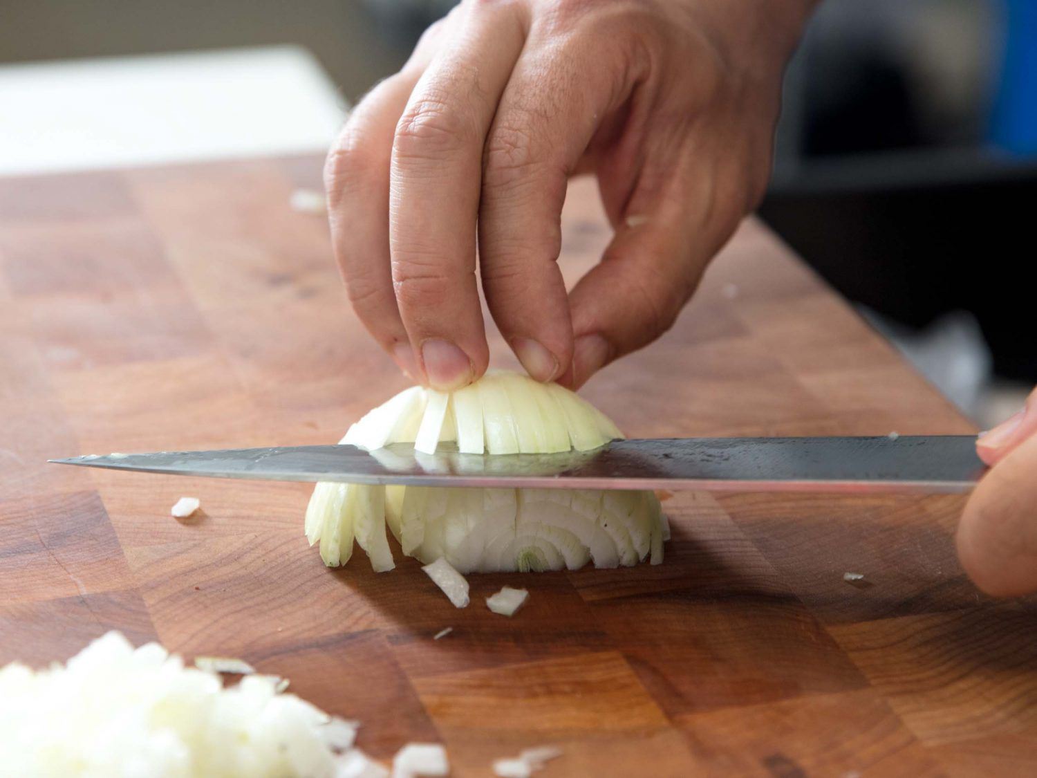 Using a chef's knife to dice an onion on a wooden cutting board