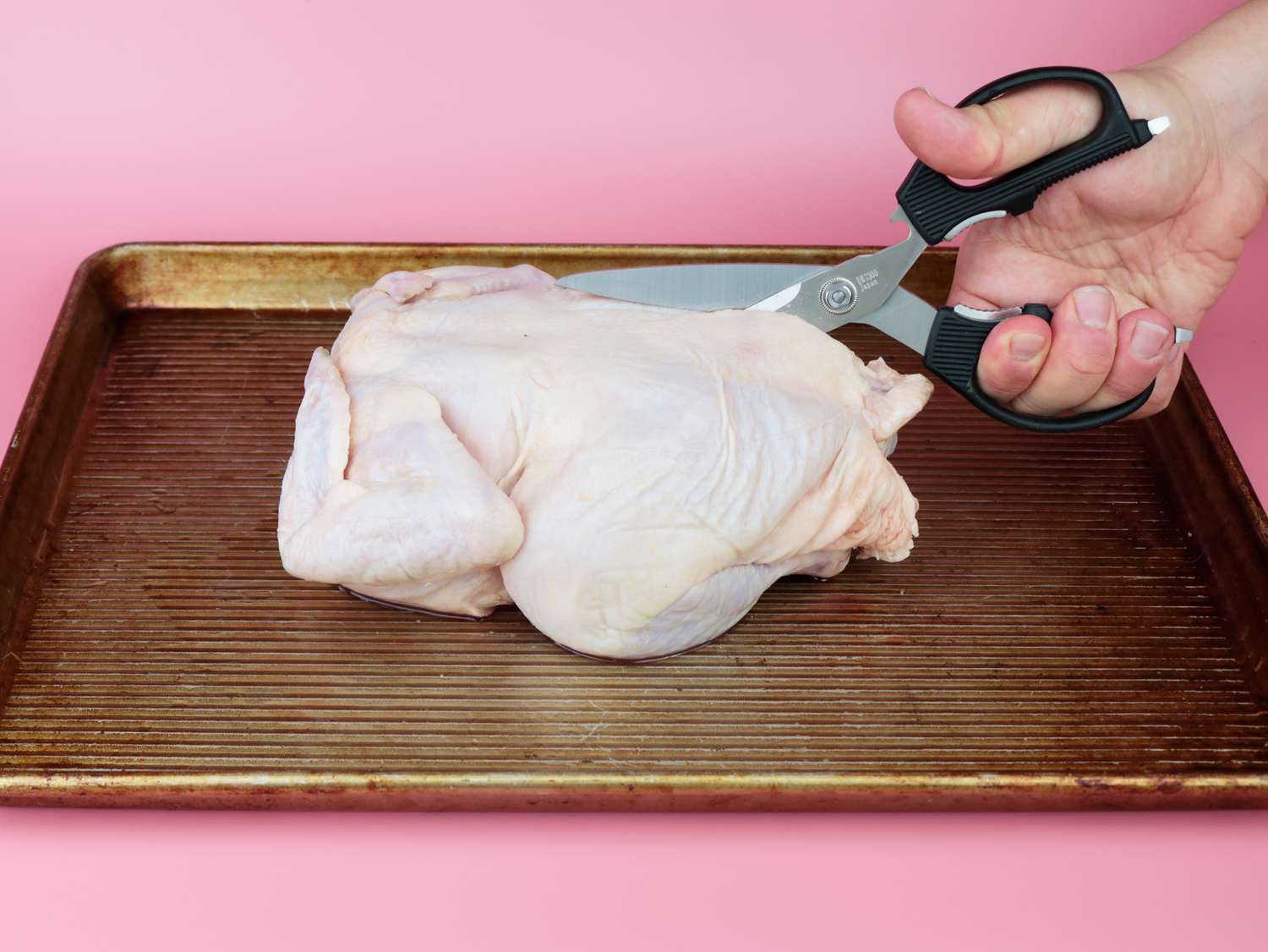 a hand using kitchen shears to cut the backbone out of a whole chicken