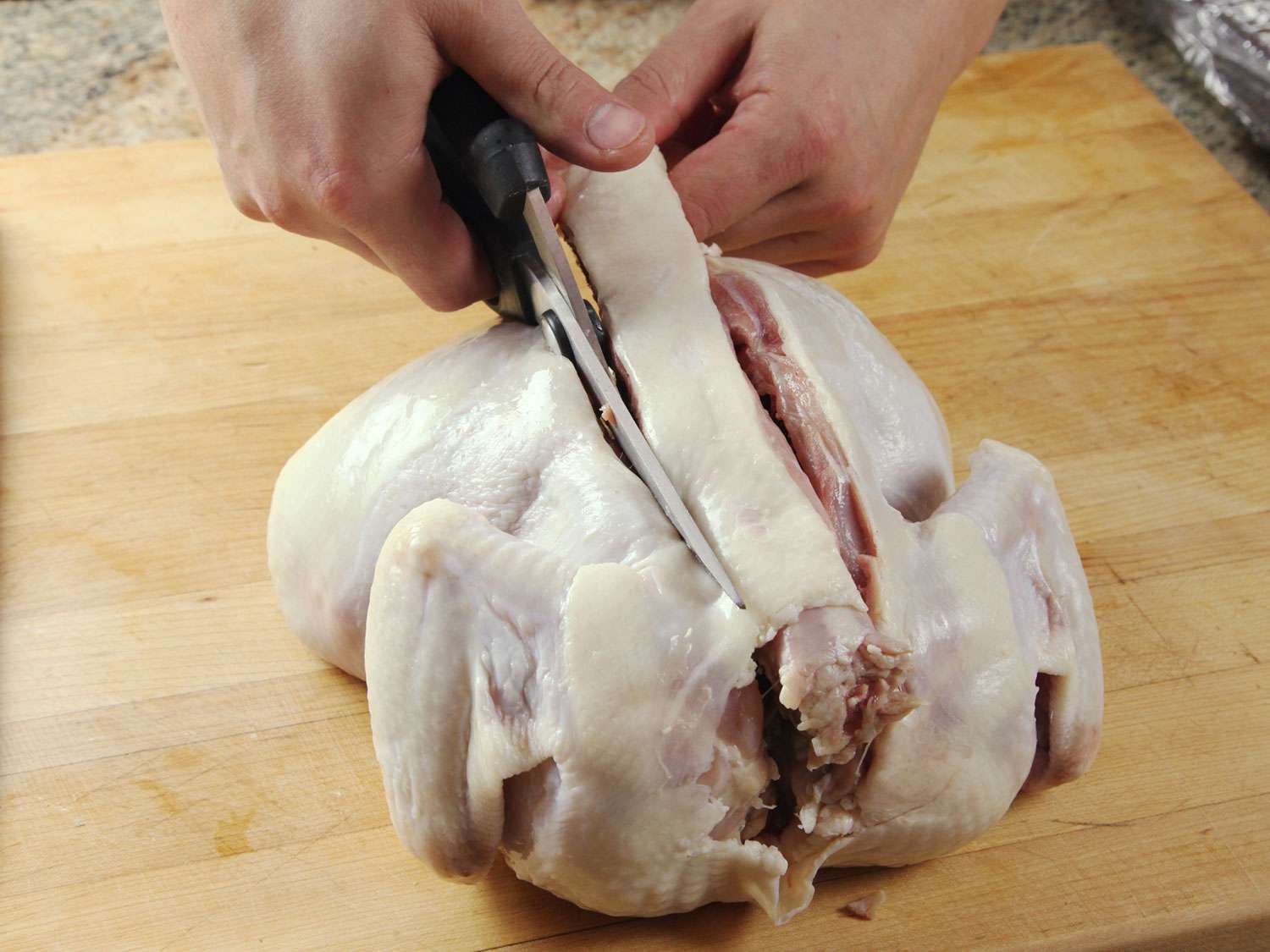 Using poultry shears to cut out the back bone of a chicken