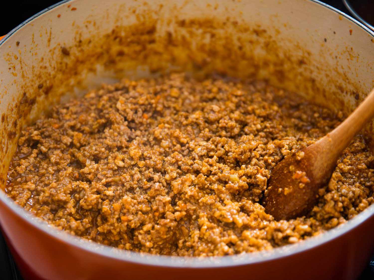 A pot of ragù Bolognese is stirred with a wooden spoon.