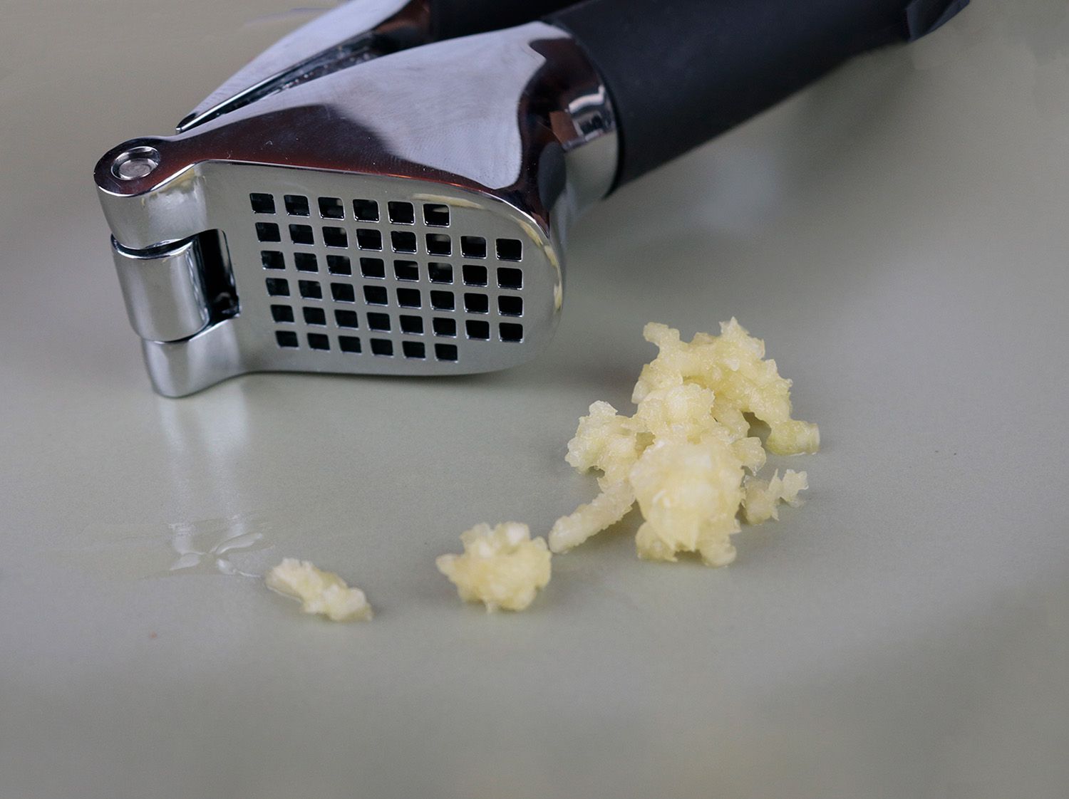 a close up of the screen of a garlic press next to a pile of minced garlic