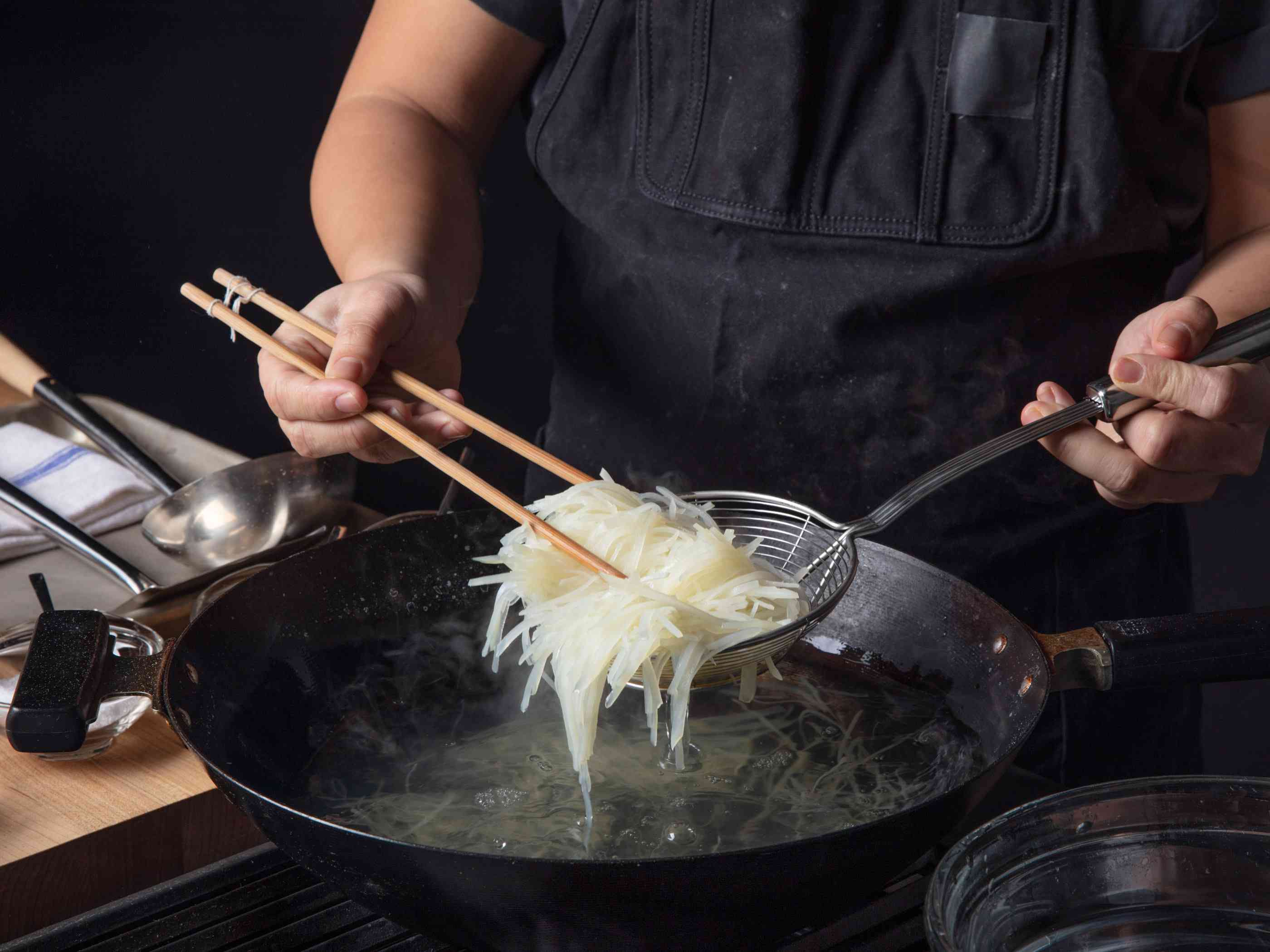 用蜘蛛和筷子将焯过的土豆条从沸水锅中捞出