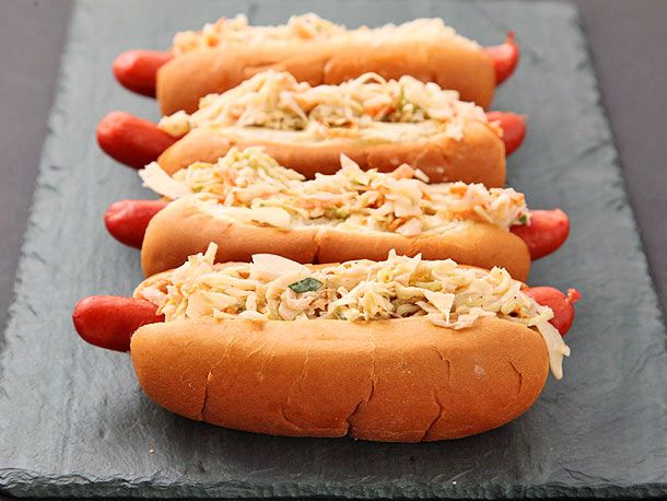 Four hot slaw dogs lined up on a black slate serving board.
