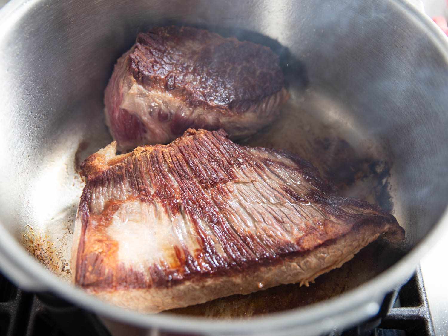 A halved brisket roast is browned in a stovetop pressure cooker.