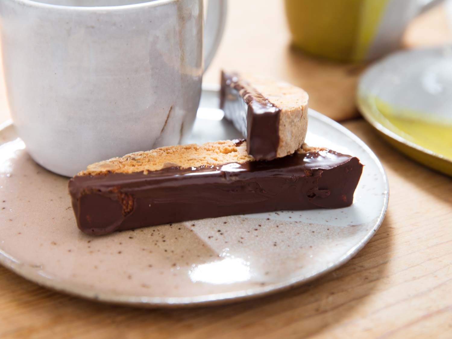 Close-up of a pair of chocolate-dipped biscotti next to a coffee mug.
