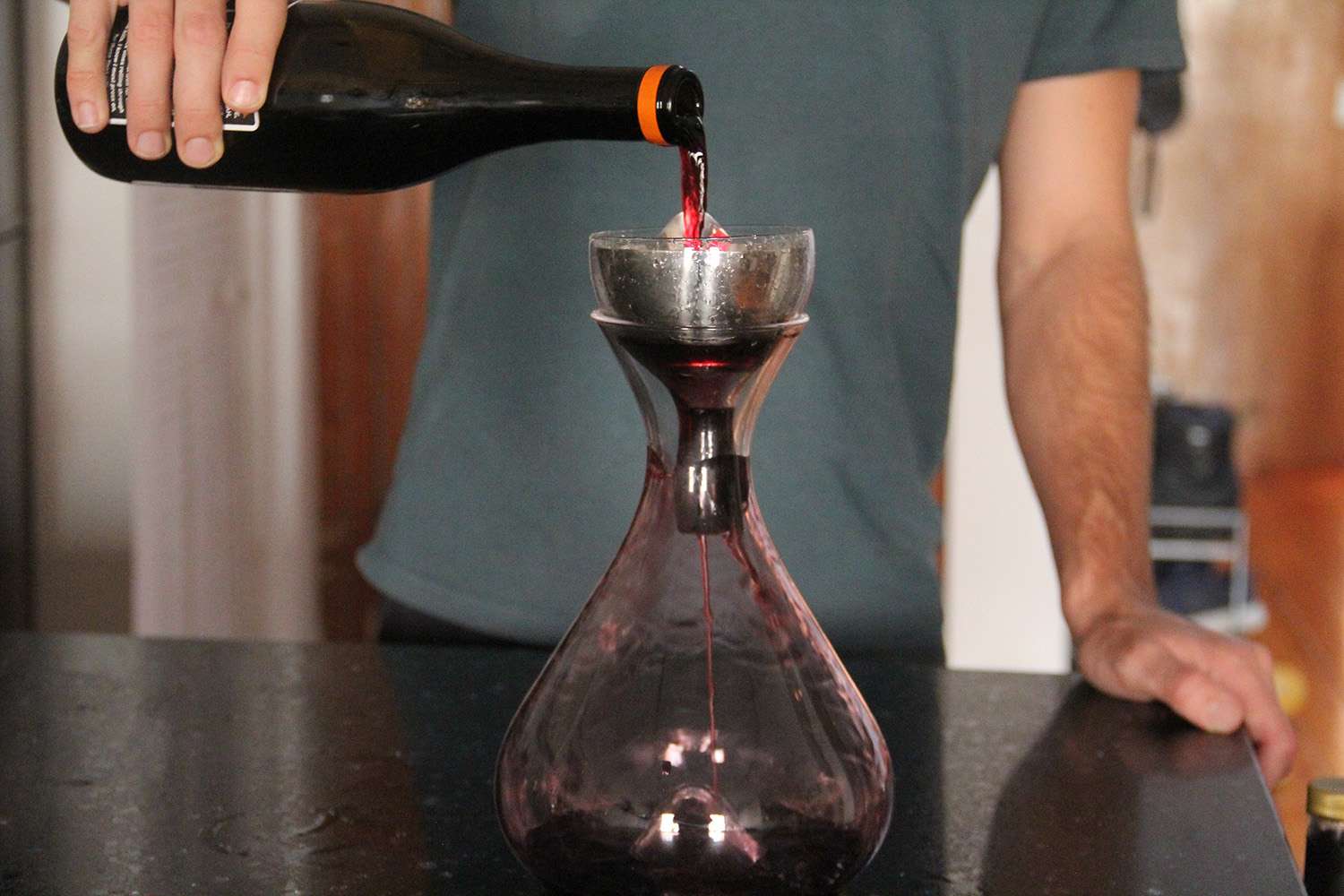 A person pouring wine into a wine decanter with a filter