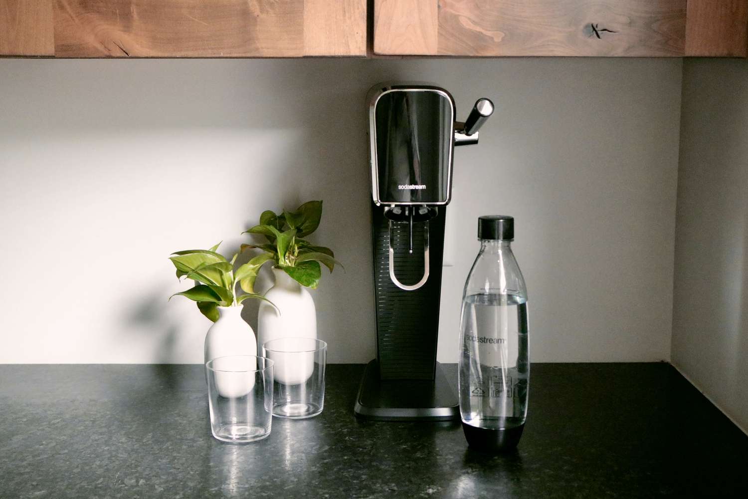 一个黑色SodaStream on a kitchen countertop with two glasses and a SodaStream bottle beside it