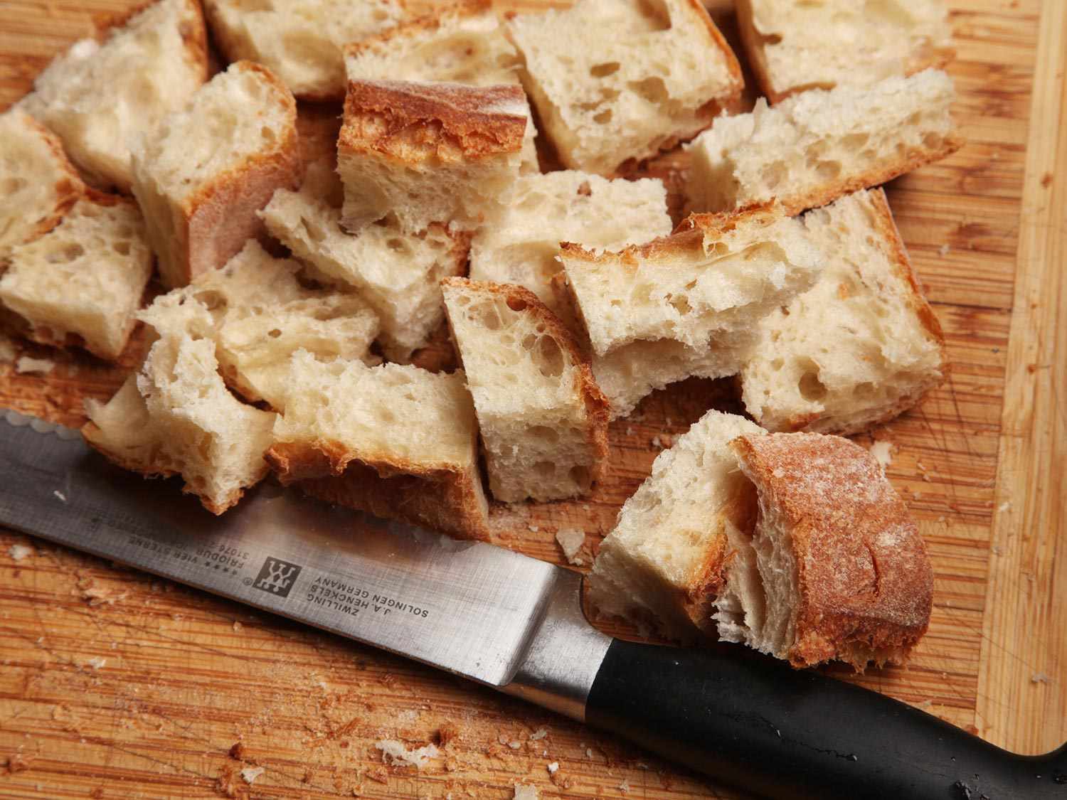 Cubed crusty bread on a wooden cutting board, next to a knife