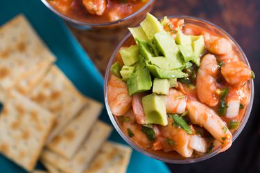 Overhead shot of poached shrimp in tomato-based sauce and diced avocado served in cocktail glass